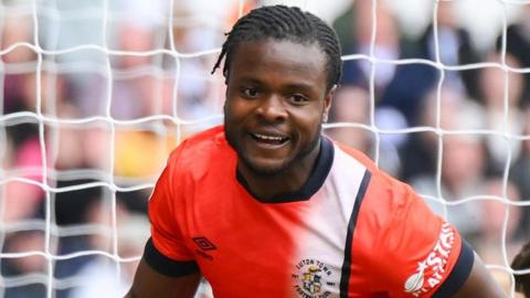 Millenic Alli in an orange and white Luton Town jersey during a match.