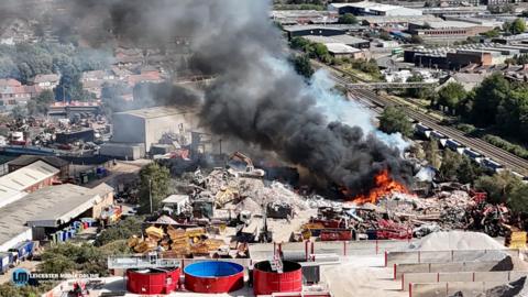Drone shot of flames and smoke coming from an industrial yard.