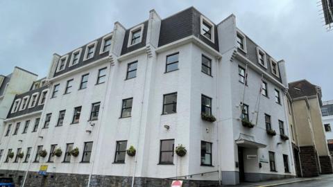 A four-storey white building on a corner block under a cloudy sky.