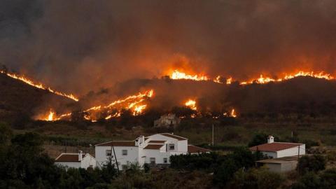 Flames tear through the hills around houses.