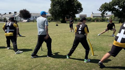 A group of cricketers with disabilities go through a stretching exercise wearing yellow and black kit 