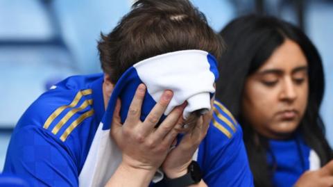 A fan looks dejected, face covered by a scarf
