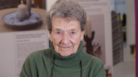 Hedi Argent sits facing the camera, wearing a green jumper, with display boards behind her.
