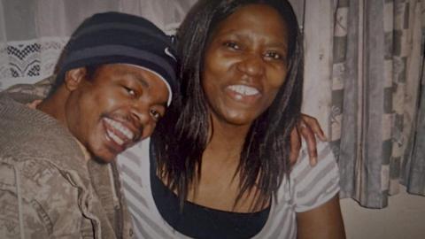 A smiling Julius Matera, with a grey and blue Nike beanie hat and a brown jacket, poses for a photo with his arm around his auntie, who has long black hair and a white top. 