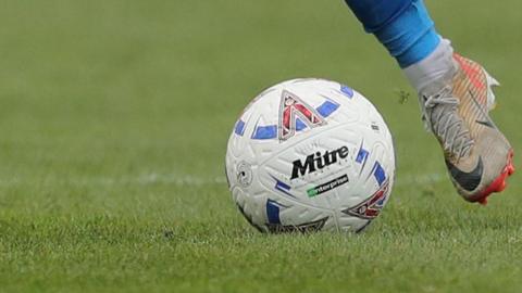 A National League ball with HUFC written on it, being kicked by a white boot with a blue sock