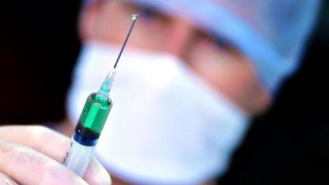 A doctor with a syringe. A drop of liquid is coming out of the needle.