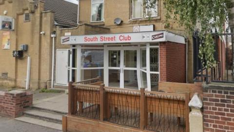 A former working men's club entrance, with three steps, wood and metal railings lead from the street. 