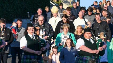 pipers lead a crowd down a street