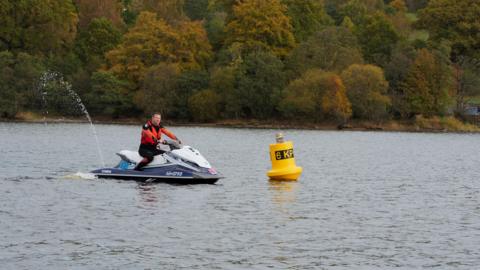 A man on a white and blue jet ski, riding it near a buoy 