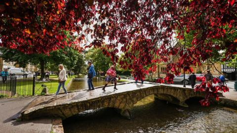 People walking over a bridge over water on an autumn day in Bourton-on-the-Water, Cotswolds