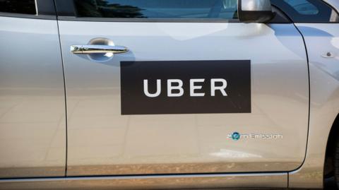 The side of a silver car with a black 'Uber' sign and the words 'zero emission' below it.