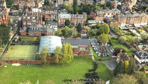 An aerial view of a largely grassy area, with playing fields, sports pitches and a large domed building, surrounded by smaller buildings