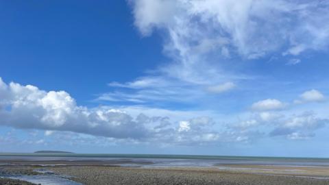A line of shower clouds amid blue sky above a pebbled beach 
