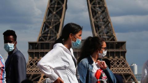 People wearing protective face masks walk at the Trocadero square near the Eiffel Tower in Paris