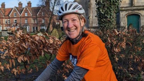 Clare Gore wearing an orange t-shirt and helmet smiling on her bike