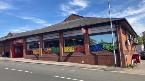 A shopfront with pictures of fruit in the window and an orange and red signage which reads "Iceland".
