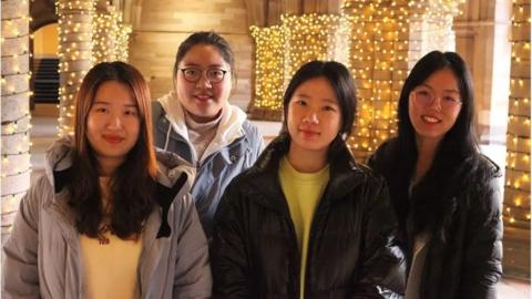 Four Chinese students standing in Glasgow University cloisters where fairy lights are attached to the pillars 