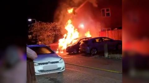 A car parked in a driveway is on fire at night