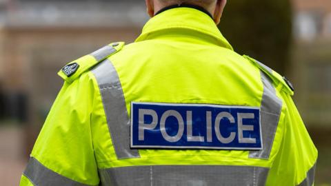 The back of a high-vis police jacket. The police officer is facing away from the camera. 