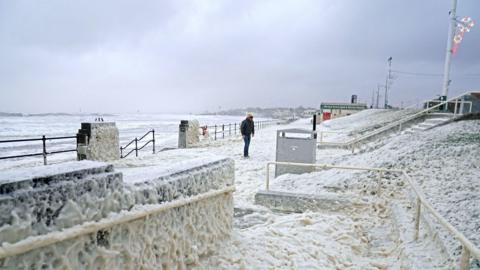 A man walks through sea foam in Seaburn, Sunderland, as Storm Babet batters the country.