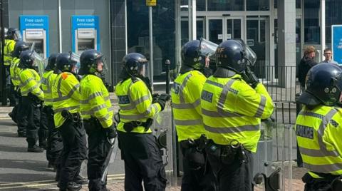 A row of police officers with helmets and yellow reflective jackets standing in the street