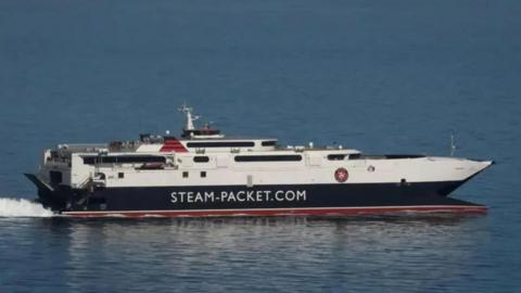 The Manannan fast craft ferry sailing on calm blue waters. The vessel is painted in the Steam Packet livery of red, black and white and has Steam-Packet.com on the side in large white lettering.