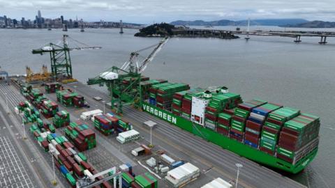 A green container ship loaded with containers sits docked at the Port of Oakland by two cranes on June 07, 2023 in Oakland, California.