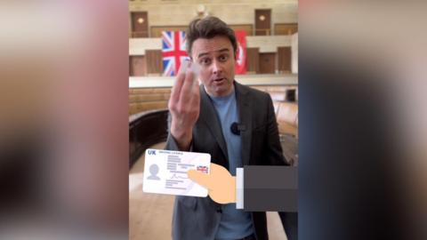 Simon Dedman wears and blue t-shirt and formal jacket in council chamber