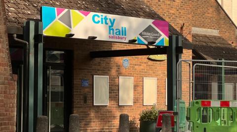 One of the entrances to Salisbury City Hall, with a sheltered area around the door which is set into a 1960s red brick building. Sign above it reads City Hall Salisbury