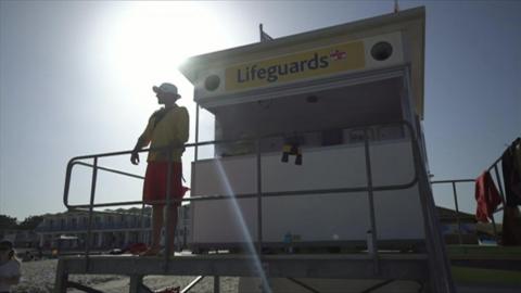 A lifeguard stood looking out towards the sea, in front of his lifeguard station