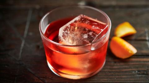 A red liquid and large ice cube in a glass