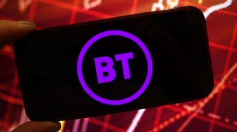 The purple BT logo of the letters "BT" inside a circle is seen on a smartphone being held in landscape. Behind it is a stylised bar chart with red lines on a darker red background