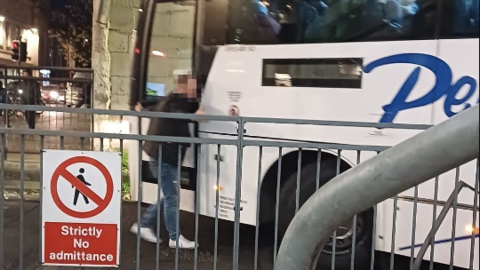 Picture shows image of a man standing very close to a white bus. He is attached and his face is blurred. 