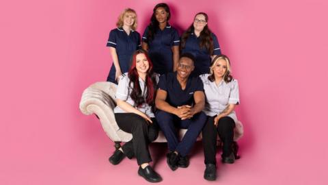 Six midwives from the documentary sit on a sofa with a pink background behind them