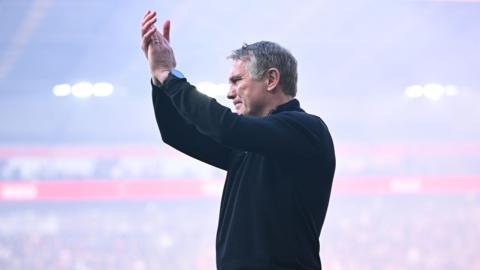 Phil Parkinson applauding wearing a black jacket and a black watch