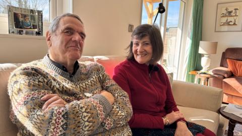 David and Anne Strobel sitting next to each other on their sofa at home looking happy after the court case went in their favour.