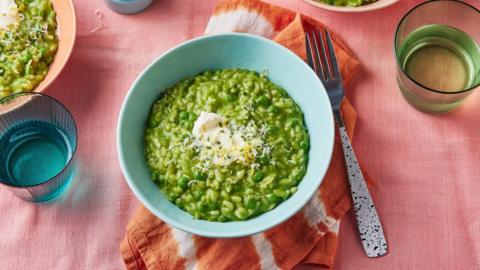 Pea risotto in a bowl on a pink tablecloth 