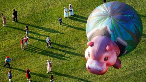 A baby hippo balloon is watched by visitors to a balloon festival