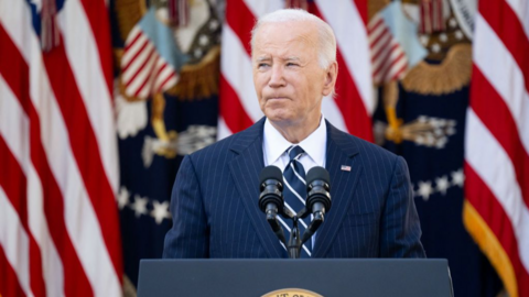 Joe Biden wearing a suit speaking at a microhpone