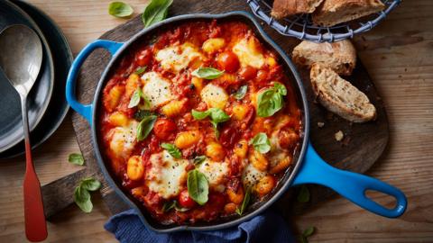 Top down view of a blue pan with one handle containing tomato and mozzarella gnocchi bake.