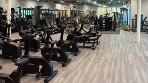 Rows of cardio machines in a gym. There are several cross fit machines and stationary bikes.