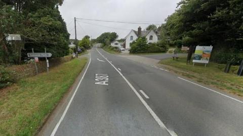 A road junction with grass and trees either side. A sign points towards Oaklands Park.