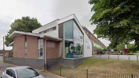 A building behind a fence with a silver car towards the front of the image