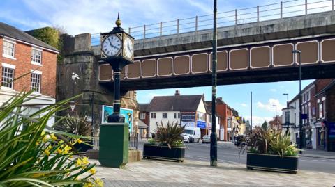 A town centre street with a clock on a pillar, a railway bridge and a road junction