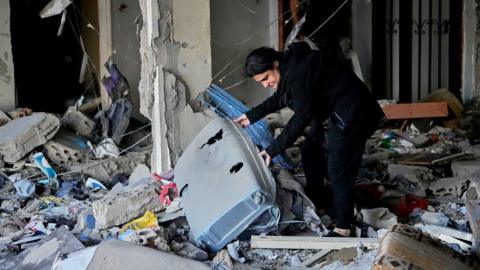 A woman lifts a damaged suitcase as she checks rubble in a destroyed apartment that was hit in an Israeli airstrike in the southern port city of Sidon, Lebanon on Thursday