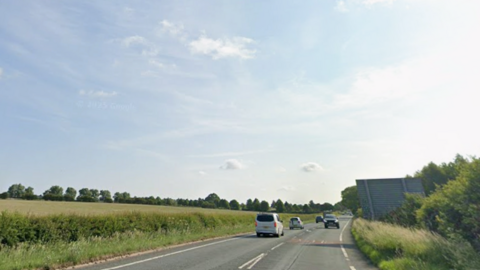 Road with a field to the left of the image, with blue sky above