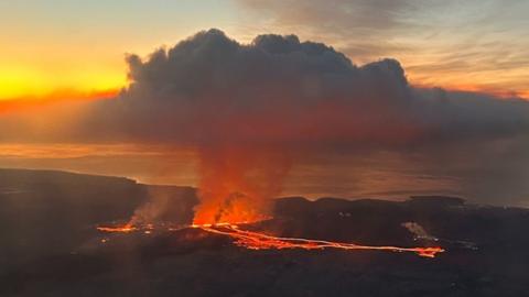 A volcano can be seen erupting including a large plume of smoke above it.