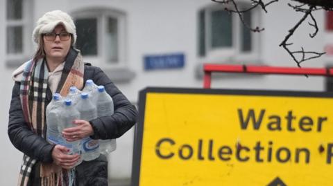 A woman lifts bottled water from a stack of bottled water
