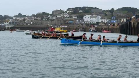 A side-on image of a crews sat in two gigs with oars out of the water as they race.