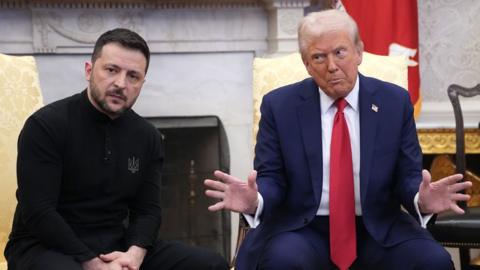 Volodymyr Zelensky and Donald Trump sit side by side meeting in the Oval Office.  Donald Trump is making an open hand gesture 